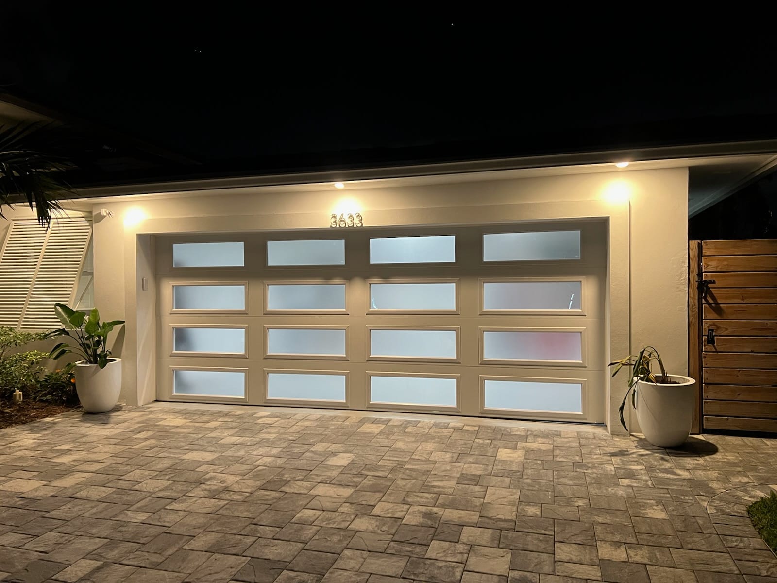 Full-view frosted glass garage door lit at night on a paver driveway in South Florida