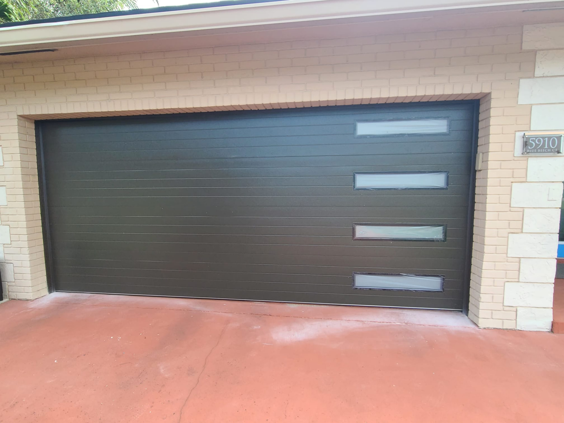Charcoal flush panel garage door with narrow frosted windows on a brick home