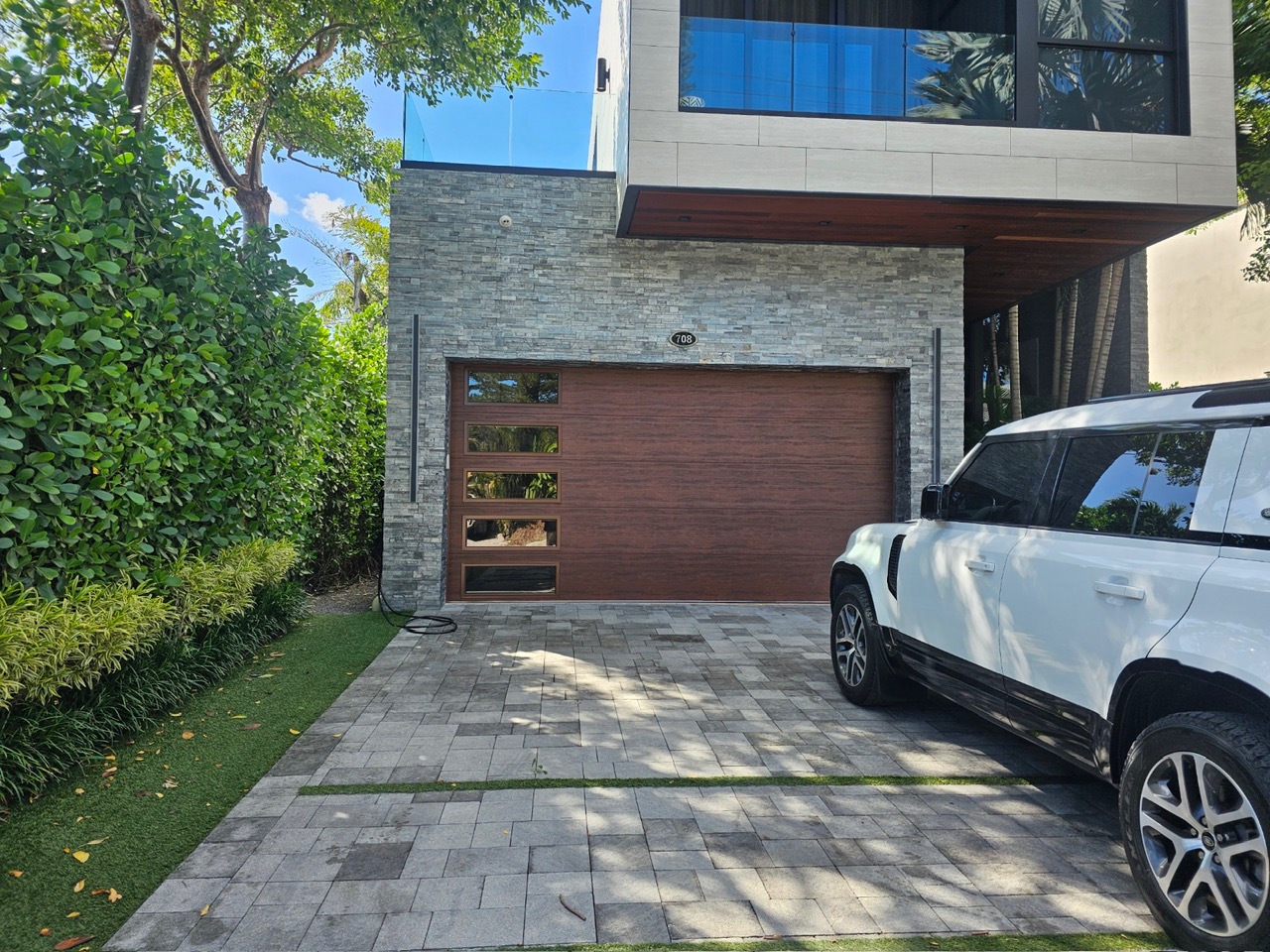Mahogany woodgrain garage door with vertical glass window row and paver driveway